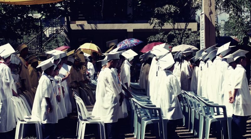 Group of children in academic gowns celebrating graduation outdoors.
